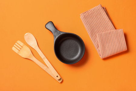 Kitchen utensils and dishcloth on orange background, cooking and home decor flat lay