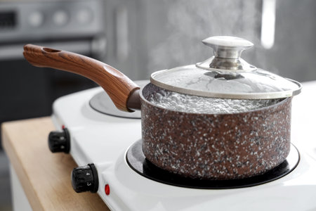 Saucepan with boiling water on stove in kitchen, closeup