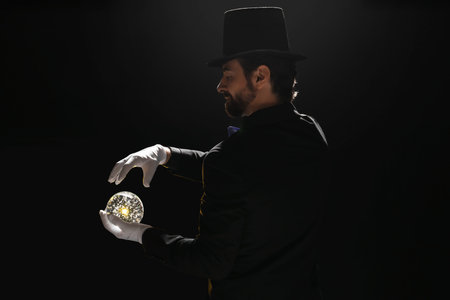 Male magician with crystal ball on dark background