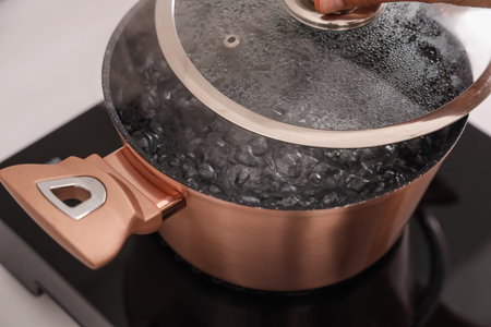 Cooking pot with boiling water and steam on electric stove in kitchen, closeup