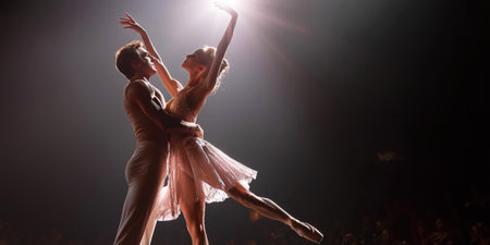 A male ballet dancer lifts a girl ballerina in his arms on stage illuminated by a bright spotlight. They showcase elegance and poise while captivating the audience in a nighttime performance.の素材