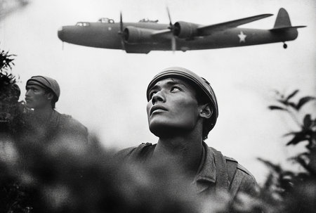 Two soldiers watch intently as an aircraft flies overhead in the midst of intense military operations during War in Malaya showing tension and focus of battle.の素材