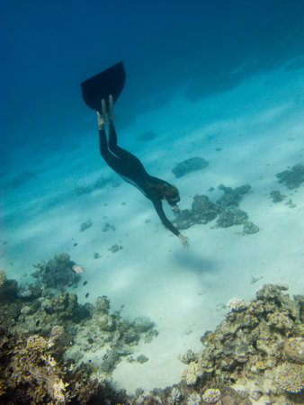 Freediver girl dives toward sand sea bottom near the coral reef in Red Sea