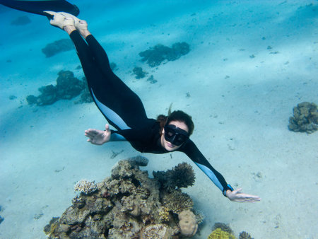 Beautiful girl with monofin looks toward underwater camera near the coralの写真素材