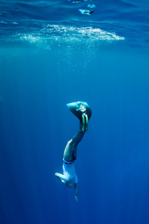 Freediver starts her dive to the sea depth from the surface at the sunlightの写真素材