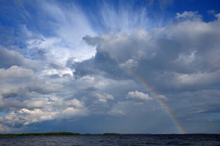Picture shows saturated and colorful rainbow under beautiful cloud in the sky over lake's surfaceの写真素材