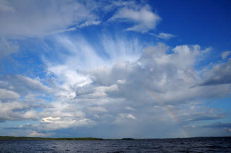 Picture shows saturated and colorful rainbow under beautiful cloud in the sky over lake's surfaceの写真素材