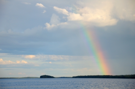 Picture shows saturated and colorful rainbow under single cloud in the sky over lake's surfaceの写真素材