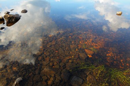 The bottom of the lake with a lot of stones and reflected skyの写真素材