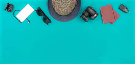 Travel and vacation accessories on the turquoise background. Travel hat, camera, passports, wireless headphones, sunglasses, power bank, AC adapter.の写真素材