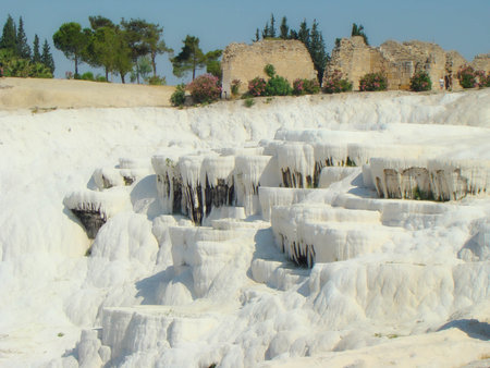 View of the snow-white travertines of Pamukkale and the ancient stone walls. Turkey. Trees in the distance.の写真素材