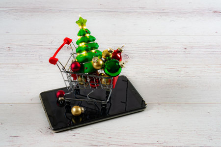 Shopping trolley with christmas balls and tree with garlands on the tablet. plain background.