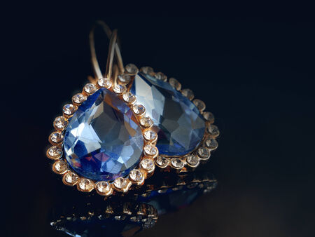 Gold ear rings against a dark background. Close up. Diamonds. Two objects. Reflection from a surface. Indoors. Color. Horizontally.の写真素材