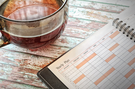 The opened notebook and glass, transparent cup of tea on a wooden table. Horizontal format. Indoors....