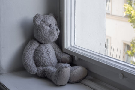 Teddy bear sadly looks out of the window onto the streetの写真素材