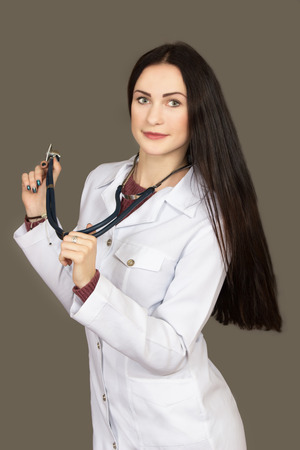 the young woman the doctor in a white scrub with a stethoscope on a gray backgroundの写真素材
