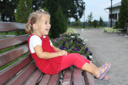 the little amusing girl in a red dress on a bench in parkの写真素材