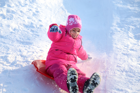 girl riding on snow slides in winter timeの写真素材