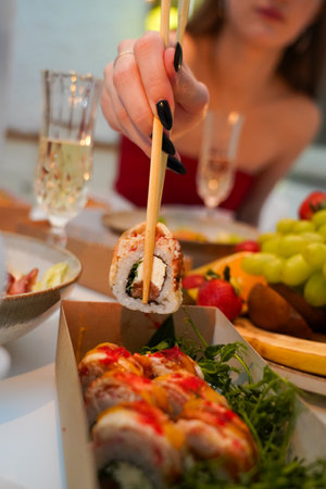 Close-up of female hands holding chopsticks with delicious sushi rollsの写真素材