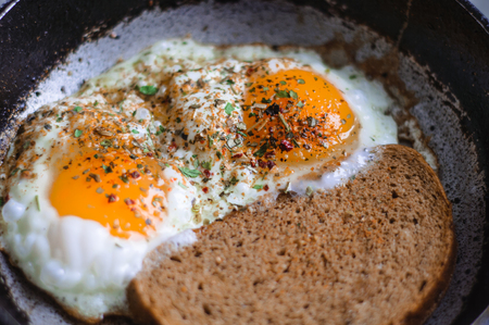 Fried eggs with bread in a frying pan and sprinkled with seasoningの写真素材
