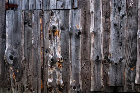 A wall made of old, darkened, frayed gray wooden knotty planks.の写真素材