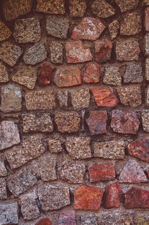 Vertical background from the Old darkened from time to time wall with granite roughly treated stones of red gray and yellow shadesの写真素材