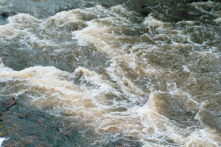 Background, top view, fast flowing river with dark blue-brown water and white foam wavesの写真素材