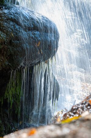 Water flowing from waterfall to stones closeup. Outdoors. Unprocessed granite stones with sprouted green moss from high humidityの写真素材