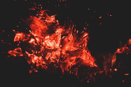 Glowing bright colorful orange-red embers bonfire. Burning coals. Warm bonfire. Horizontal photo. Close-up. Bright fire. Dim fire. Red flame. Dim dark background.の写真素材