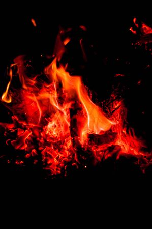 Bright fading bonfire in night summer forest. Hot embers shine brightly in dark. Warm, atmospheric evening by fire. Vertical photo. Black background. Close-up. Beauty of flame and fiery coals.の写真素材