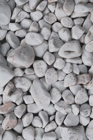 Background rounded polished white smooth stones. Decorative beautiful white pebbles. Various textures. Riverbank. Beach. Outdoors. Marble pebbles. Small river stones. Close-up. Vertical photo.の写真素材