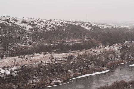 Panoramic view from shore near river on winter day. Picturesque landscape of river bank in cold season. Cloudy weather. Beautiful winter landscape. Cold morning. First snow. Horizontal photoの写真素材