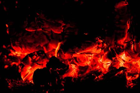Beauty of smoldering flames and coals of fire. Black background. Fading beautiful fire. Warm evening. Hot embers shine brightly in dark Horizontal photo. Outdoors. Imadge of red coals.の写真素材