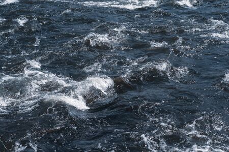 Rapidly flowing river with dark blue water, foam. Rapids river flow, sparkling in sun. Photo and texture blue water in summer. Section river with fast flow and steep channel. Horizontal photo.の写真素材