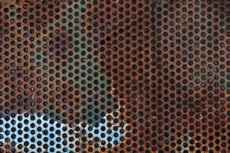 Damaged sheet metal, weathered rusted steel, grunge background with round holes, red color metal, textured surface, outdoors, horizontal close-up photo, blank template for banner design.の写真素材