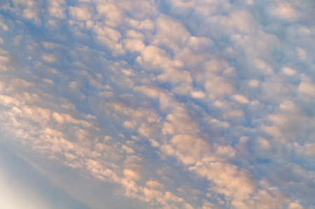 Bright blue sky, white translucent feathery clouds, reflections warm rays setting sun, swirls strong gust wind, outdoors. Horizontal photographyの写真素材