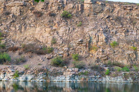 Steep bank of an abandoned quarry, stone slope with sparse bushes near the lakeの写真素材