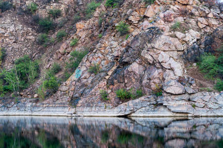 Rocky shore abandoned quarry, slope with sparse bushes near the lakeの写真素材