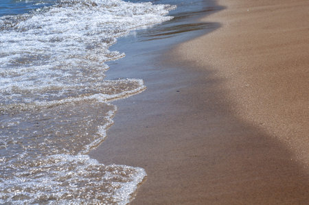 Blue sea with yellow sandy beach close-up, azure clear water, wet sandy shore.