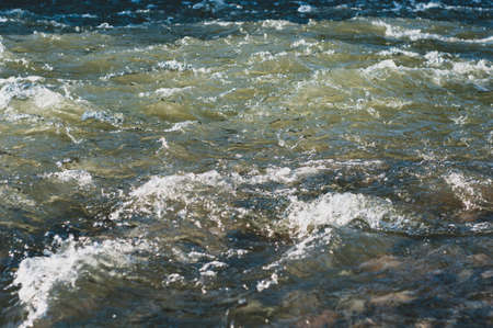 Sun glare on surface water and smooth stones at bottom stream, background. Transparent water in river with rocky bottom, fast flow. Nature outdoors close upの写真素材