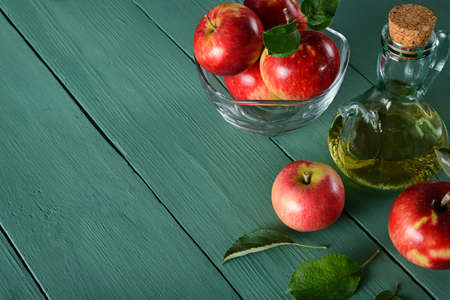 Apple cider vinegar and ripe red apples on background of green wooden table. Top view. Free space for text.の写真素材