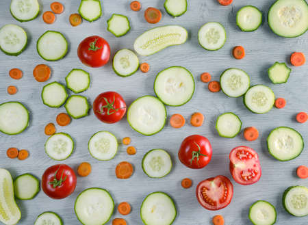 Cut vegetables on wooden background. Top view of cucumbers, tomatoes, zucchini, carrots.の写真素材
