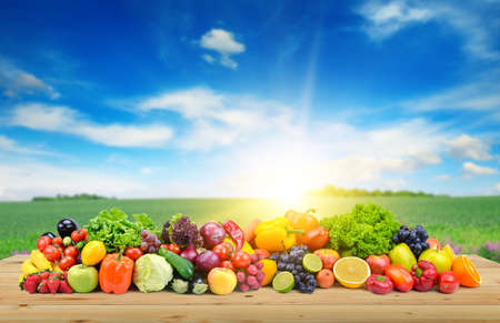 Vegetables and fruit on wooden table of boards against background of spring field and bright blue sky.の写真素材