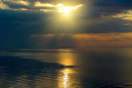 Bright sun in black clouds over ocean with sun track.の写真素材