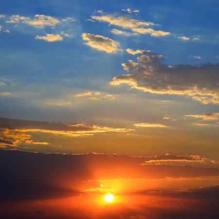 Dramatic sunset background with bright sun, blue sky and picturesque clouds.の写真素材