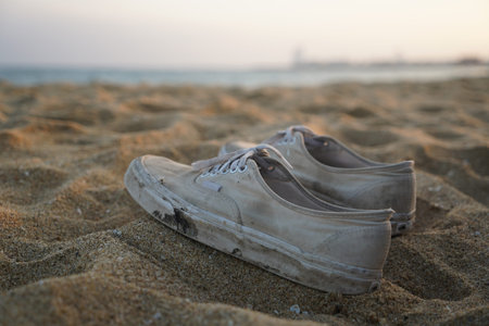old white sneakers on the sand of the beach at sunset