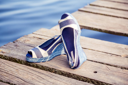 denim blue sandals lie on wooden clutch at the lakeの写真素材