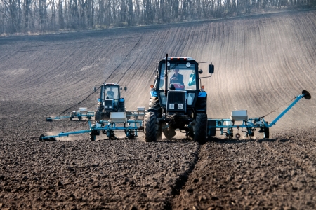 Blue tractors with sowers on the field in bright sunny spring morningの写真素材