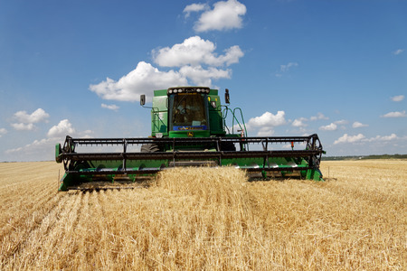 Kharkiv Region, Ukraine - July 13, 2018: Combine harvest wheat on a field in sunny summer day in Kharkiv Region, Ukraine on July 13, 2018.のeditorial素材