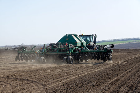 Kharkiv, Ukraine - April 10, 2019: Green tractor with trailed seeder working in field in a sunny...